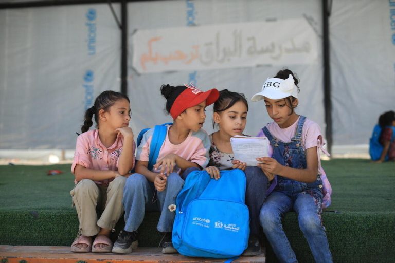 Otroci v Gazi se po letih prekinitev, izgub in opustošenja vračajo k učenju. Učenke sedijo pred začasnim učnim prostorom, z UNICEF-ovimi šolskimi potrebščinami.