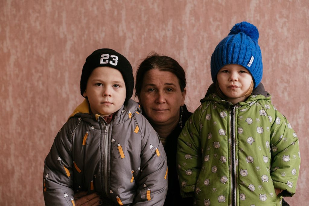 Mati iz Ukrajine z otroci pozira pred kamero. Oblečeni so v topla zimska oblačila.