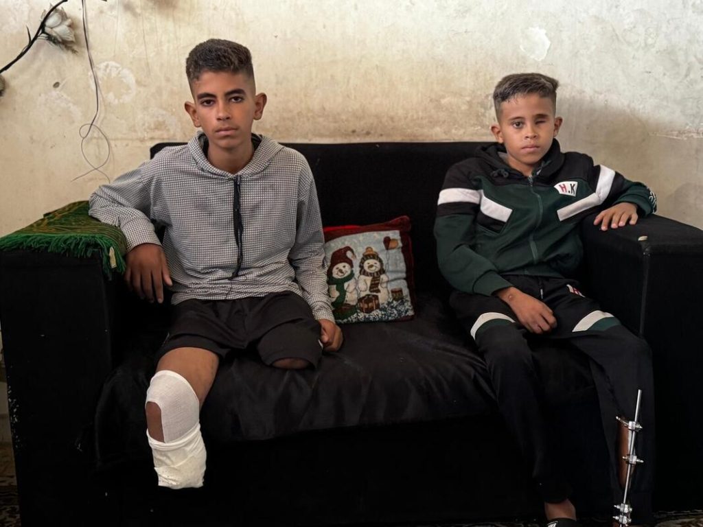 Brata Amir in Fadel iz Gaze sedita na kavču in gledata v kamero. 11-letni Amir je utrpel hude poškodbe noge, notranje poškodbe in izgubil levo oko, 14-letnemu Fadelu pa so amputirali obe nogi in še vedno trpi zaradi zapletov.