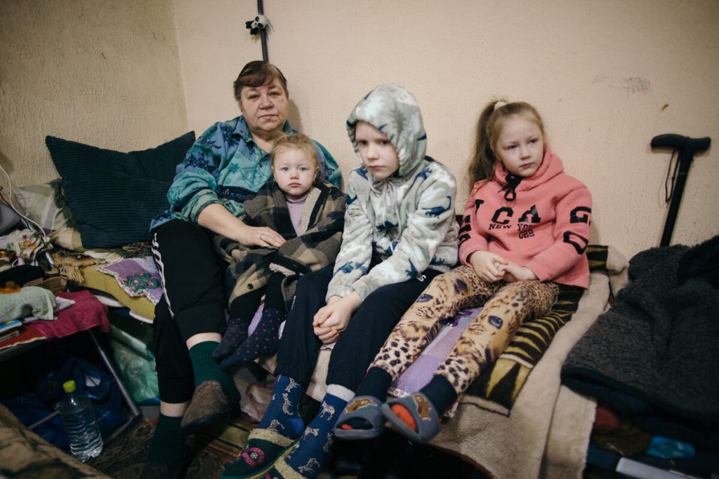 Tamara sedi s tremi vnuki v kletnem zaklonišču. Otroci sedijo tesno skupaj na postelji, zaviti v topla oblačila in odeje, medtem ko se družina pripravlja, da bo ostala v zaklonišču zaradi nenehnega obstreljevanja v bližini frontne črte.