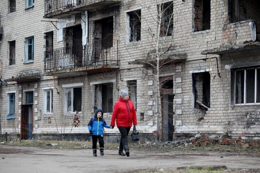 Ženska z otrokom hodi mimo stare porušene stavbe.