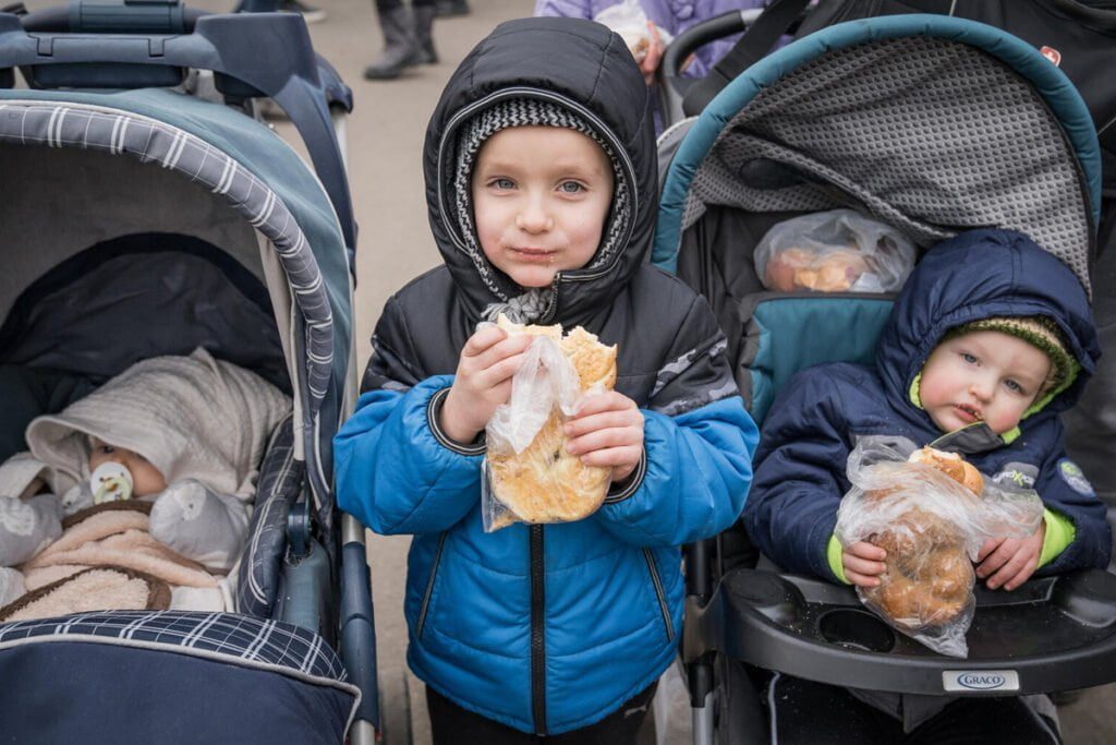 Deček, ki drži sendvič, ter dva otroka v otroških vozičkih