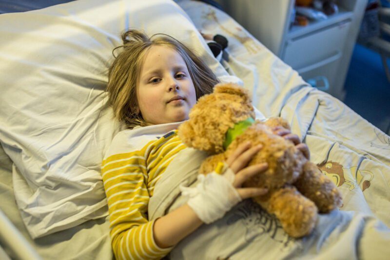 Deklica v bolnišnici s povezano roko in igračo v naročju
