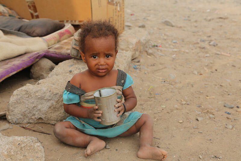 Otrok sedi na tleh s prazno konzervo v rokah