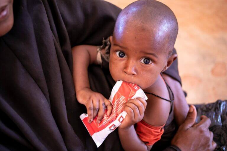Otrok iz Somalije, ki v rokah drži paketek terapevtske hrane.