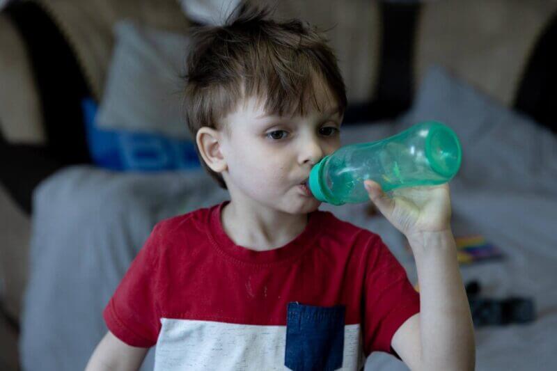Deček z rdečo in belo majico, ki pije vodo iz plastenke.