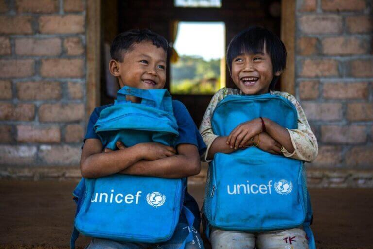 Dva nasmejana otroka, ki v rokah držita modri šolski torbi z napisom UNICEF.