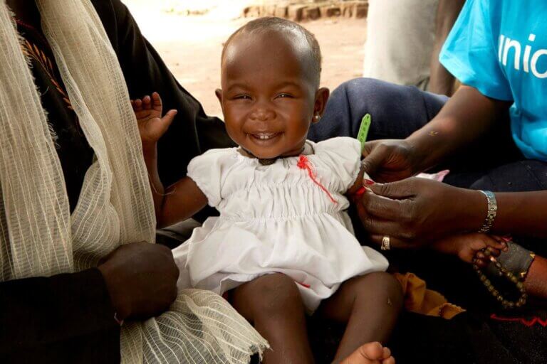 Nasmejana deklica v maminem naročju, ko ji merijo obseg roke