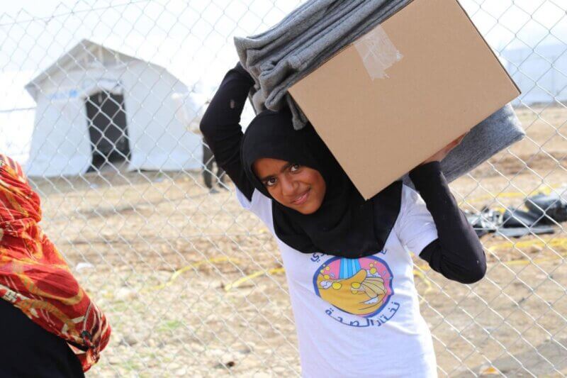 Vesela deklica nad glavo nese UNICEF-ove pakete