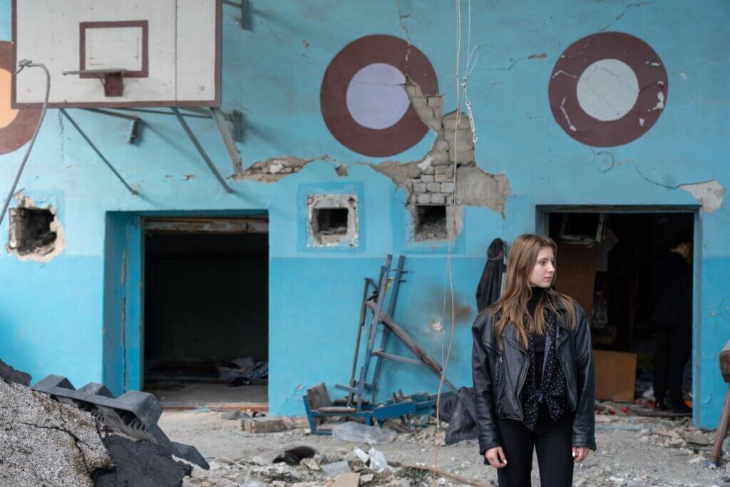 Dekle stoji v uničeni telovadnici šole.