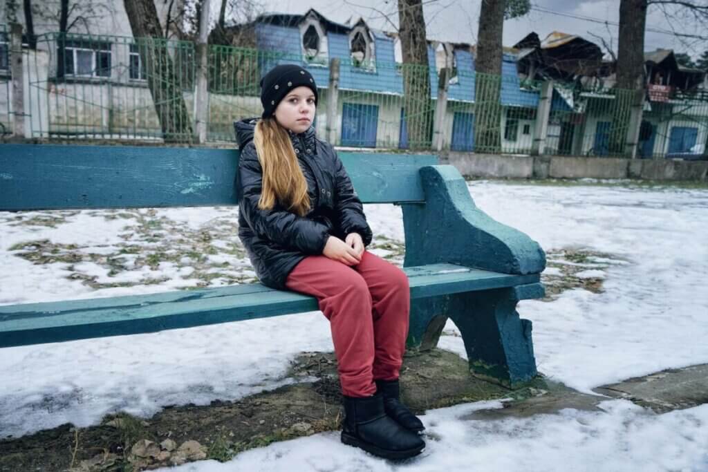 Deklica sedi na klopi v vojno razdejanem mestu Irpin.