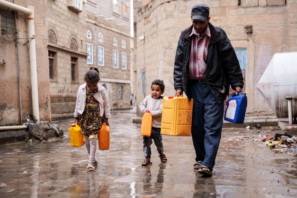Oče z otrokoma domov nese čisto vodo.