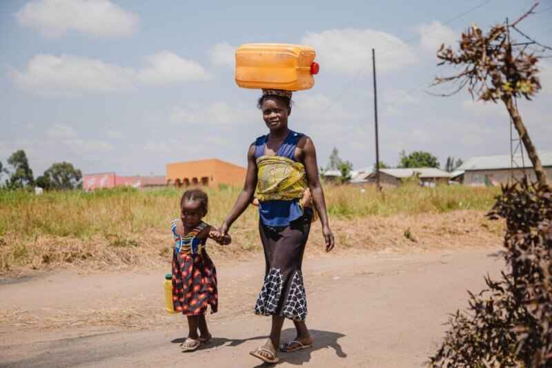 Chantale Akelo iz Sudana nosi vodo iz vodnega vira. Spremljata jo hčerka in nečakinja.