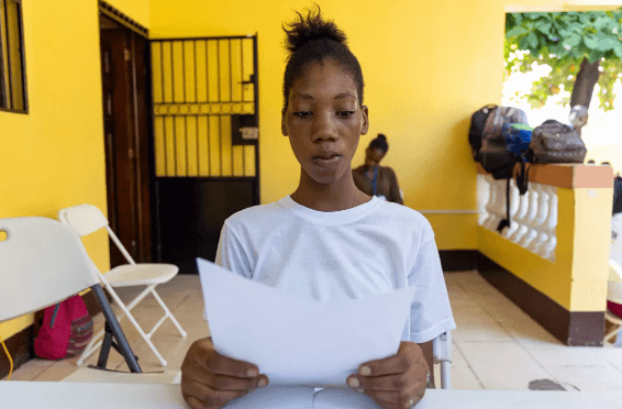 Andie iz Haitija prebira svojo pismo odraslim.