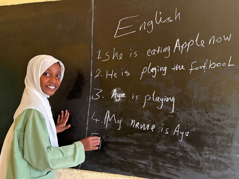 13-letna Aja med poukom angleščine na dekliški šoli Hai Alarab v zvezni državi Kassala piše angleške stavke na tablo.