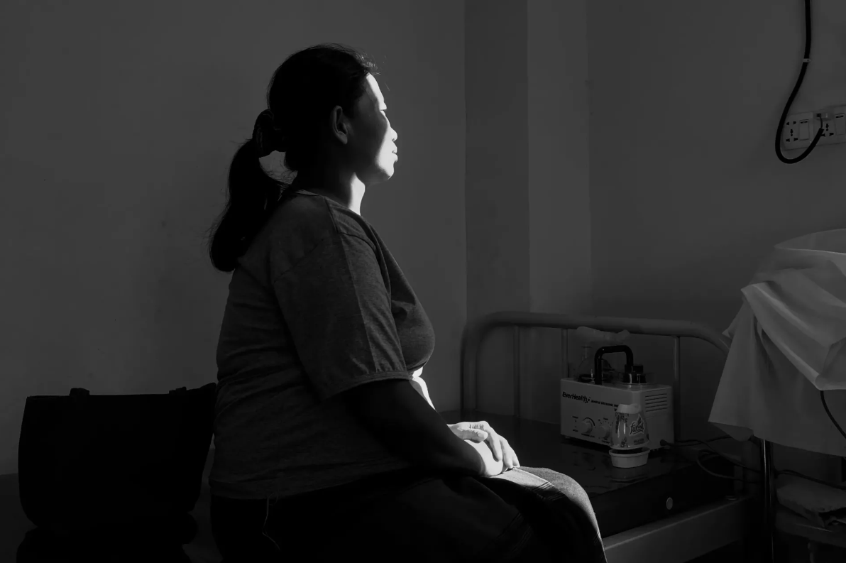 Daw Lai sedi ob oknu in z rokami počiva pred svojim nosečniškim trebuhom.