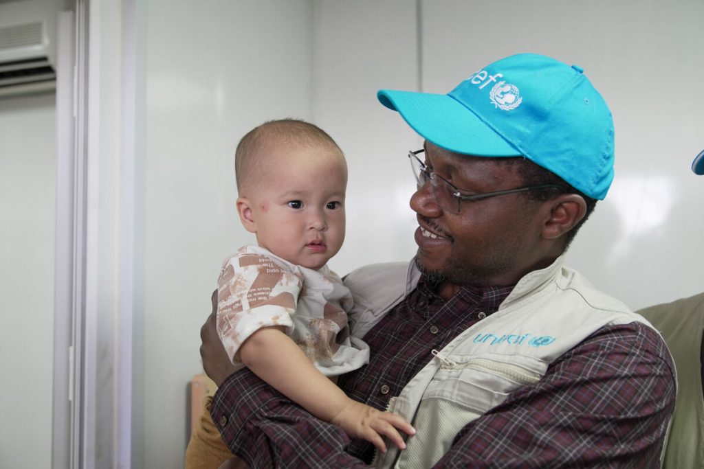 Dr. Tajudeen Oyewale, UNICEF-ov predstavnik v Afganistanu, 28. junija 2025 drži majhnega otroka, ki so mu ob prihodu v sprejemni center Islam-Kala na meji v zahodnem Afganistanu opravili pregled zaradi podhranjenosti in potrebna cepljenja.
