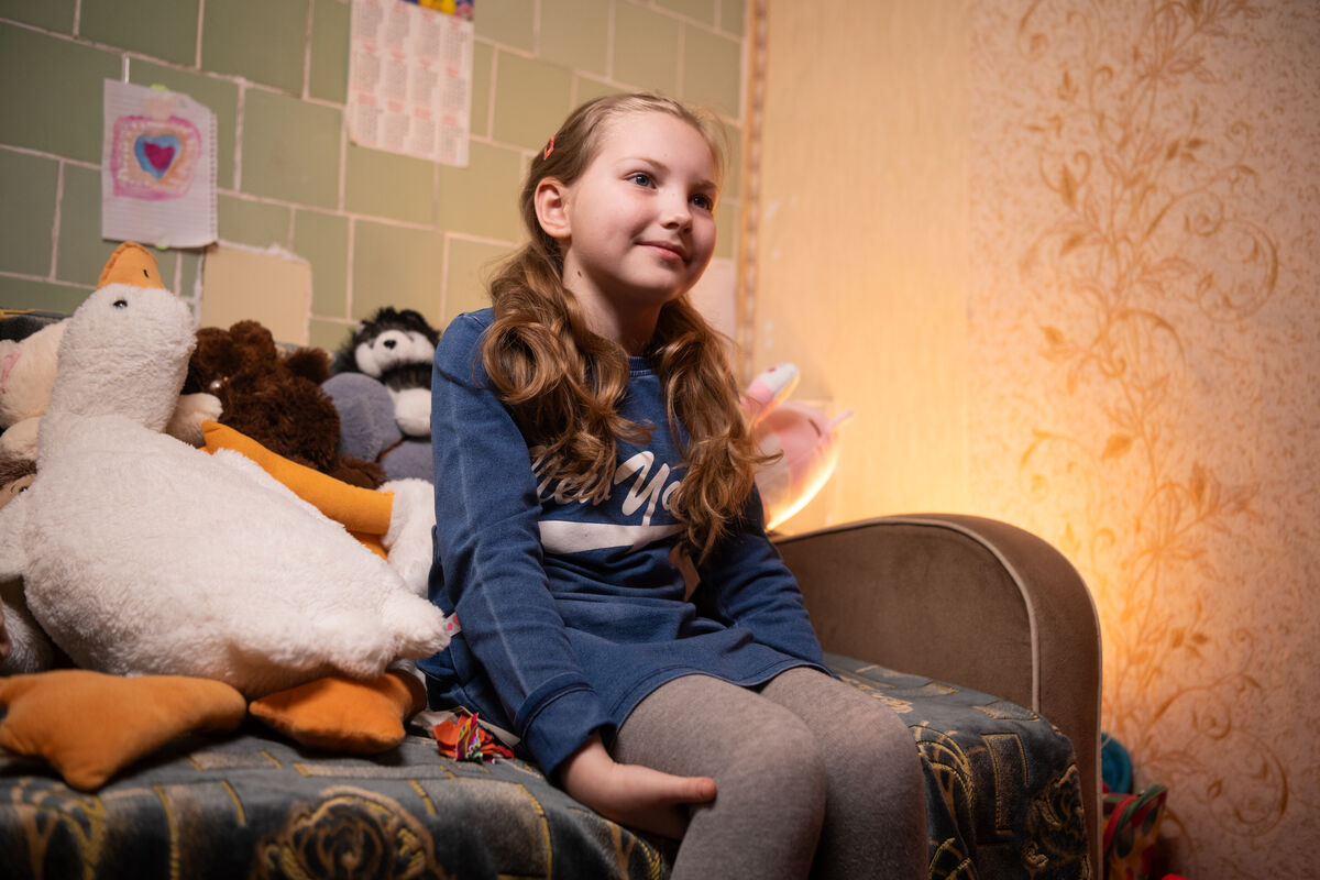 8-letna Kseniia sedi na postelji s svojimi najljubšimi plišastimi igračami in pripoveduje zgodbe o vsaki od njih.