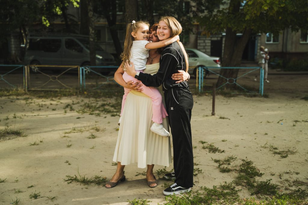 Mama Oksana objema svoje hčerki, 16-letno Katjo in 4-letno Masho, pred njunim domom v Ukrajini.