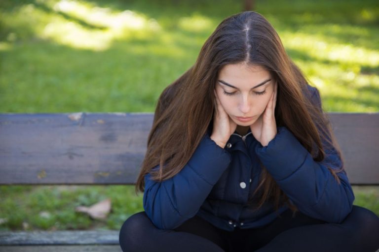 Najstnica sedi na klopi v parku.