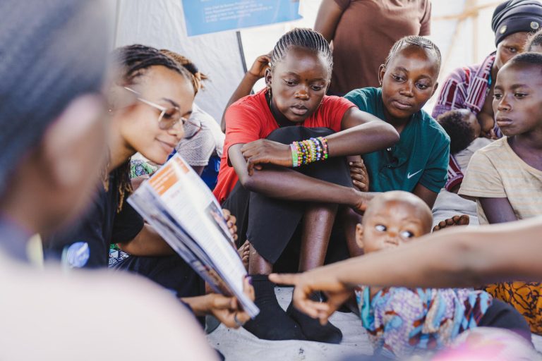 Esther N’kuba (z očali), pripovedovalka zgodb in aktivistka za pravice žensk, se pogovarja z razseljenimi ženskami in dekleti med ozaveščevalno delavnico o vzrokih in posledicah nasilja nad ženskami in dekleti.