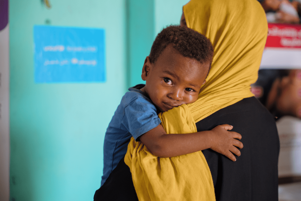 Mlad fant počiva na rami svojega negovalca, medtem ko čaka na oskrbo v zdravstvenem domu, ki ga podpira UNICEF.