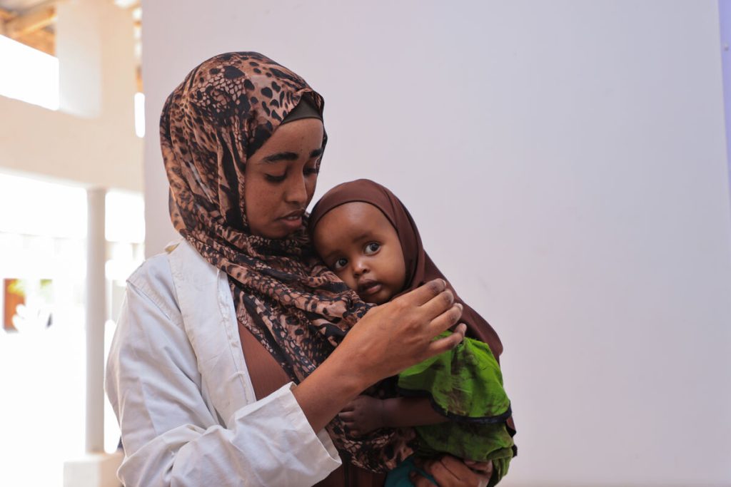 Zdravstvena delavka iz Somalije v naročju drži otroka.