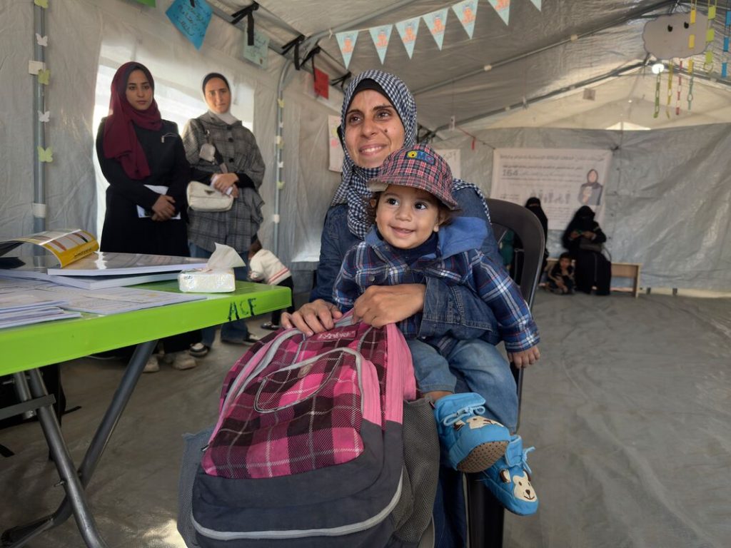 Mati iz Gaze drži otroka, s katerim sta prejela nujno pomoč. Zadovoljna se smejita kameri.