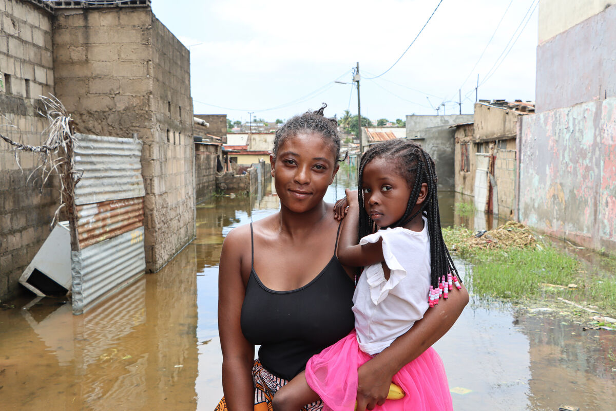 Mati pred poplavljeno ulico drži svojo hčerko v roki in pozira kameri.