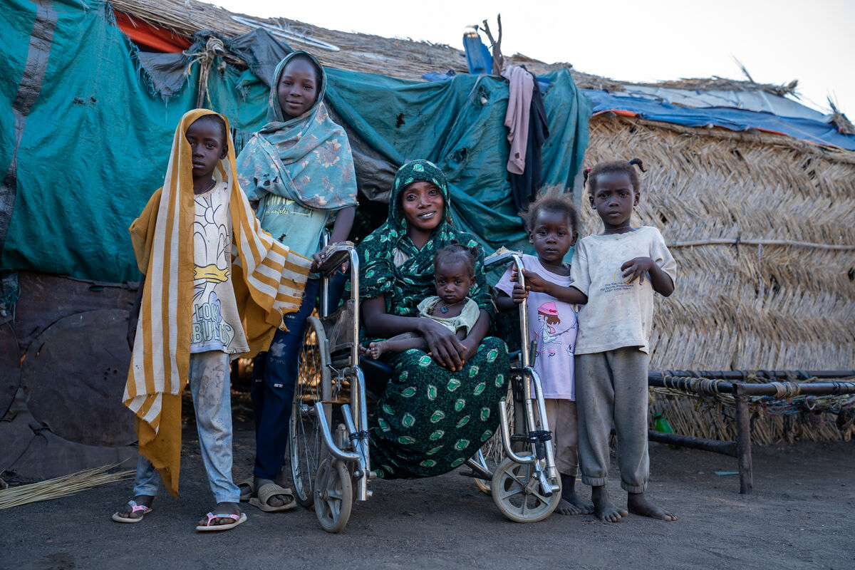 Mati z invalidnostjo pozira pred hišo s svojimi petimi otroci.