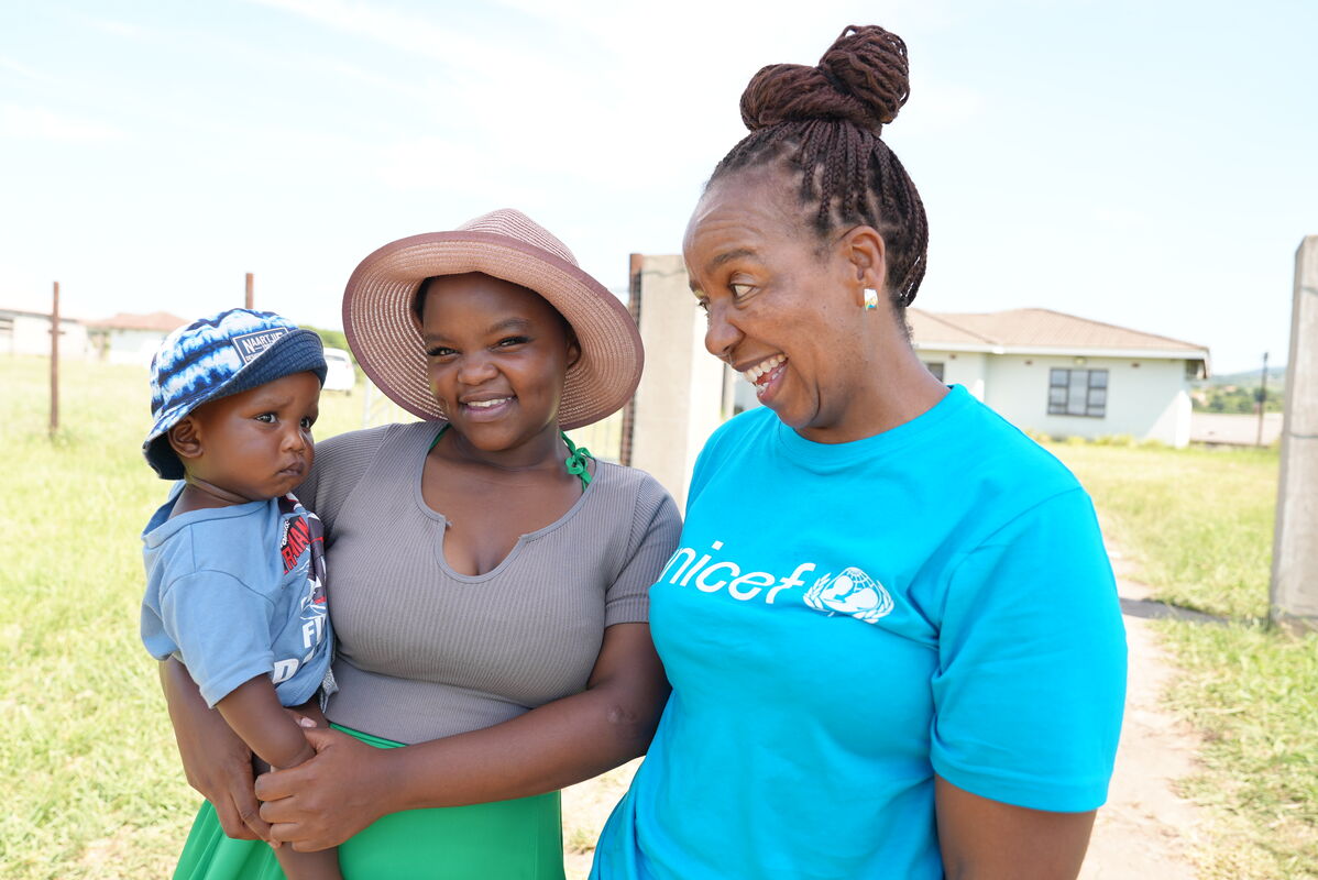 Mati drži svojega otroka v roki in skupaj z UNICEF-ovo sodelavko se smejijo kameri.