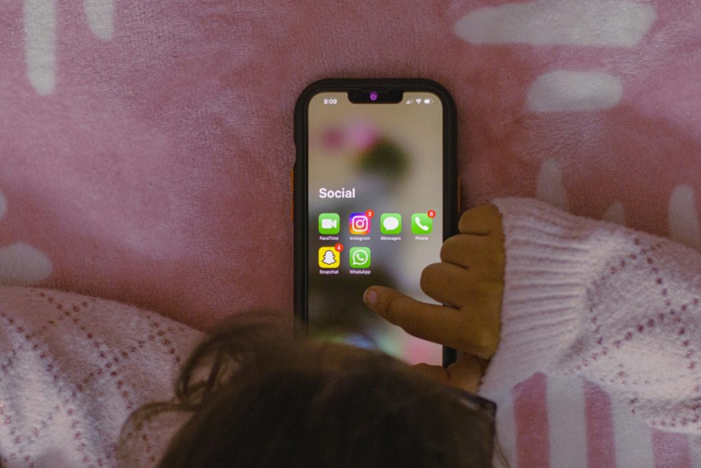 Oseba leži v postelji in drži mobilni telefon.