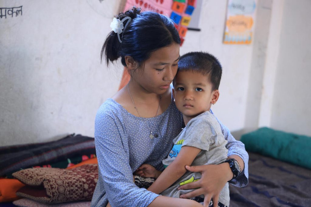13-letna Sonika nosi svojega 3-letnega brata Sajana, kjer je družina našla zatočišče po uničujočih poplavah v Nepalu.