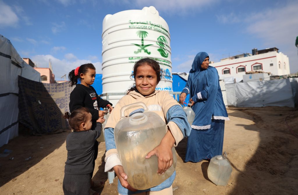 Deklica s kanistrom za vodo stoji ob UNICEF-ovem vodnem rezervoarju v zavetišču v Gazi.