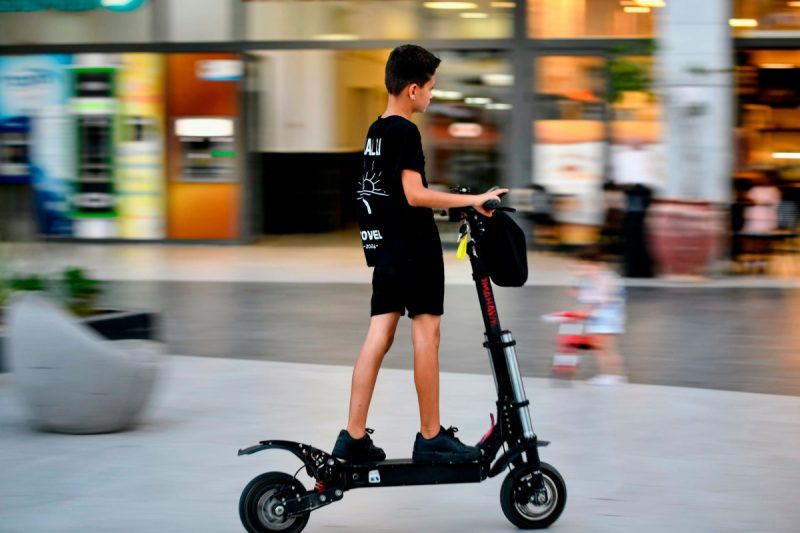 Deček se vozi z električnim skirojem na prostem.