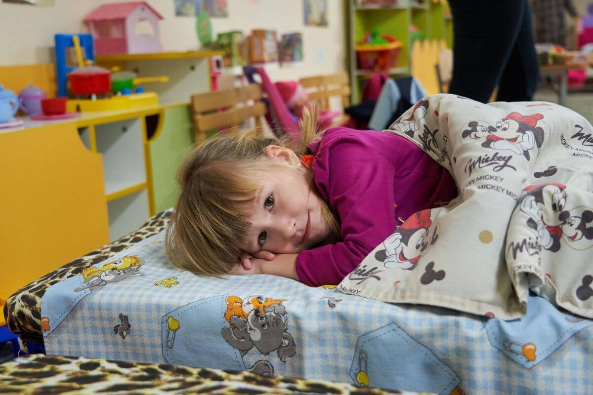 Dekle spi leži v postelji v novem zaklonišču v vrtcu v Ukrajini.