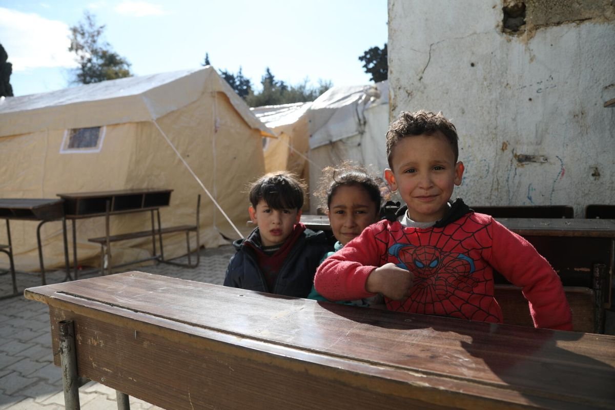 Otroci sedijo pred šotori začasnega zatočišča.