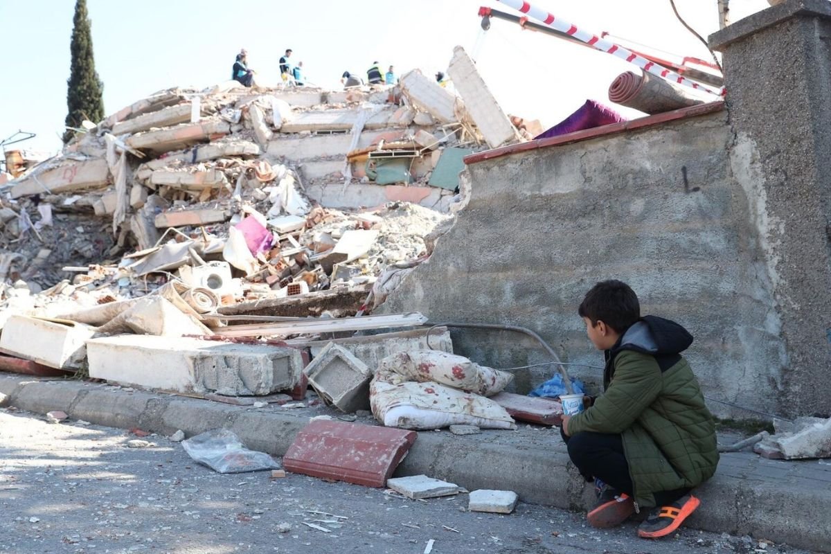Otrok gleda v ruševine in čaka, če bodo reševalci našli njegove prijatelje.