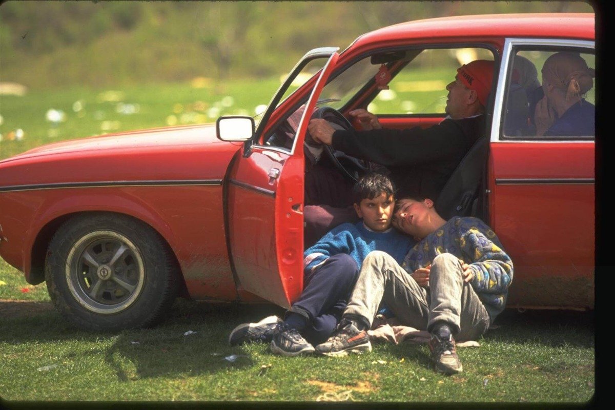 Dva otroka, ki spita na tleh ob avtomobilu.
