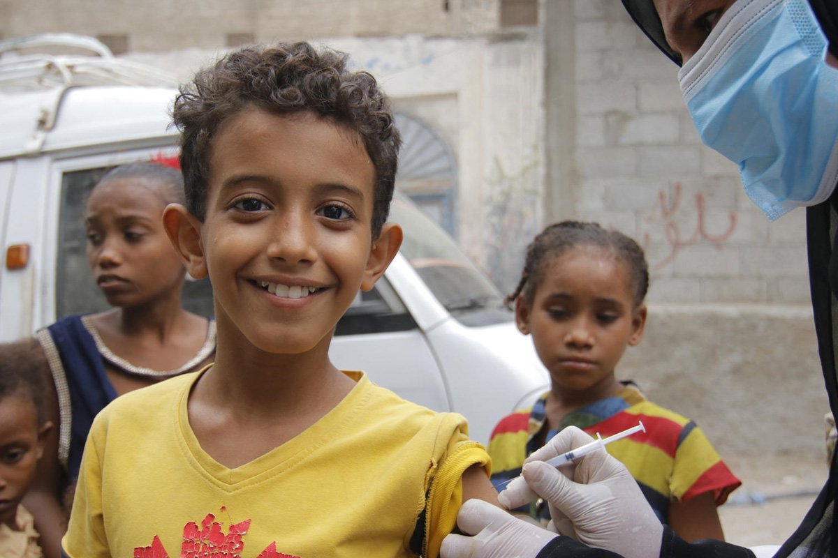 Nasmejan deček iz Jemna, ki prejema cepivo