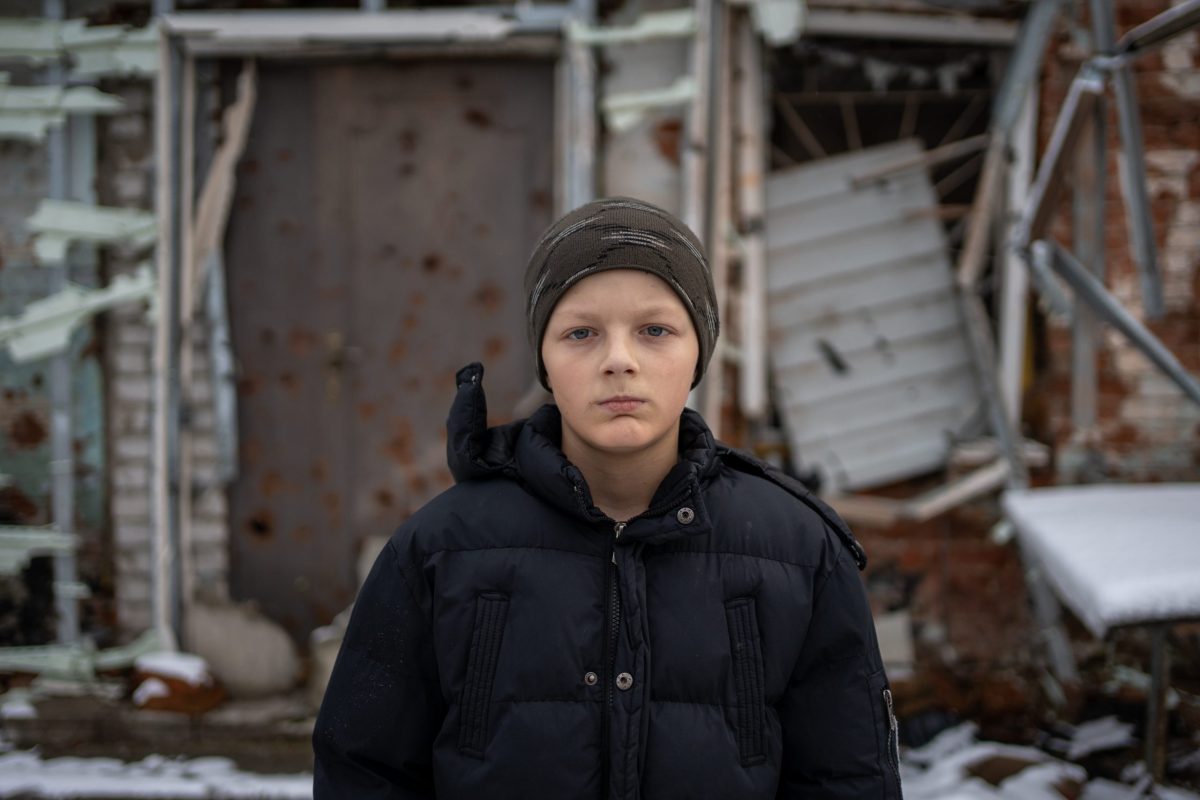 11-letni Bohdan stoji pred uničeno šolo v Ukrajini.