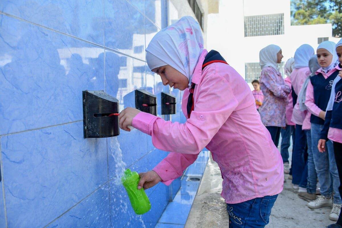 11-letna Lamis si polni plastenko vode na dvorišču obnovljene UNICEF-ove šole v Siriji.