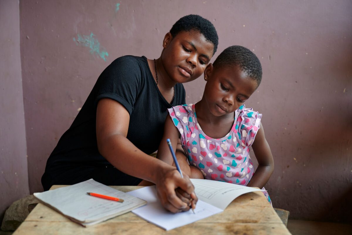 Sestrična Vera pomaga 7-letni Bennedikti pri domači nalogi pred hišo v občini Juaben v regiji Ashanti v Gani, Zahodna Afrika.