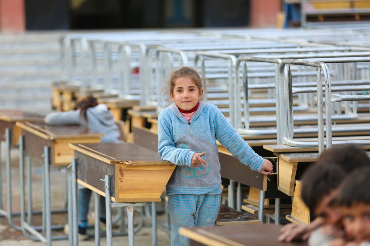 Deklica v zatočišču v Raqqi stoji med šolskimi mizami. Z družino je pobegnila pred stopnjevanjem nasilja v Alepu na severu Srije.