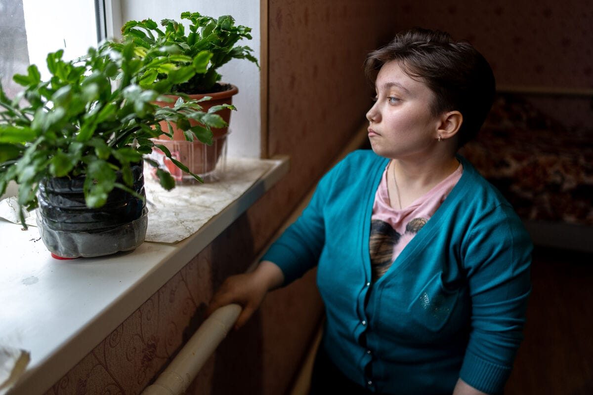 18-letna Darina iz Ukrajine gleda skozi okno svojega majhnega stanovanja. Na okenski polici svetita kaktusa, kar ji prinaša veselje v težkih časih.